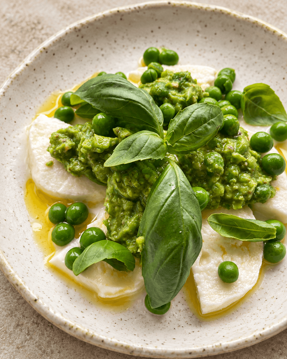 Slices of mozzarella with pea and basil pesto puree, whole peas and a sprig of basil