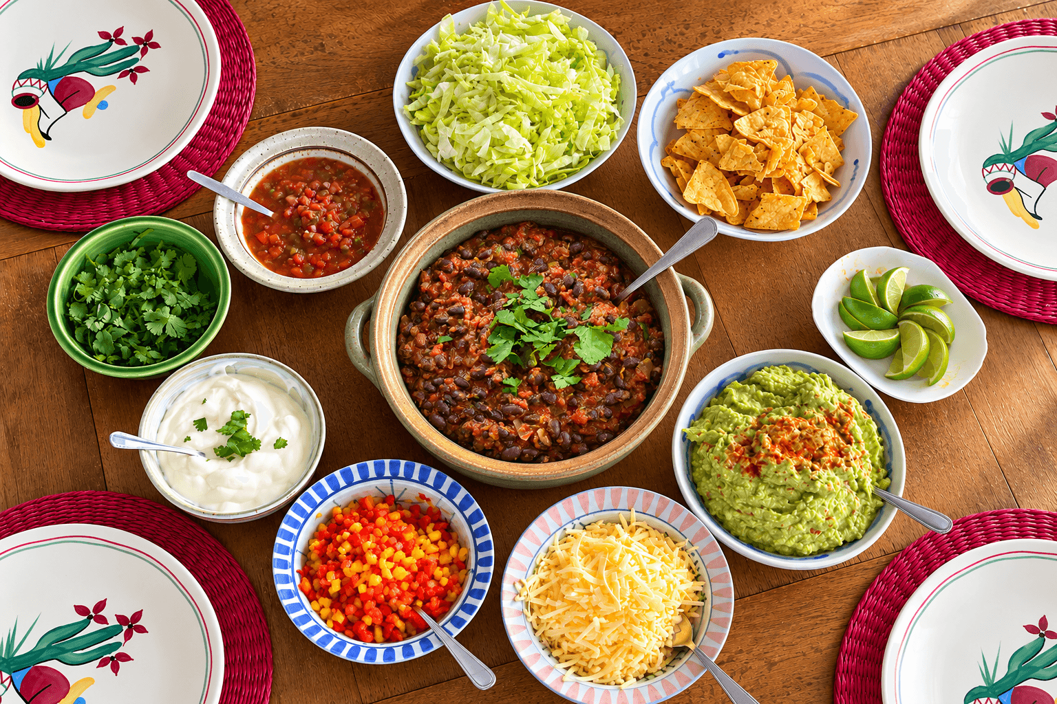 Bowls of burrito fillings; cheese, lettuce, black bean chilli, guacamole, cucumber, tomatoes, capsicum, sour cream and lime wedges